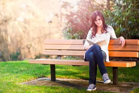 Ragazza legge libro su panchina in un parco